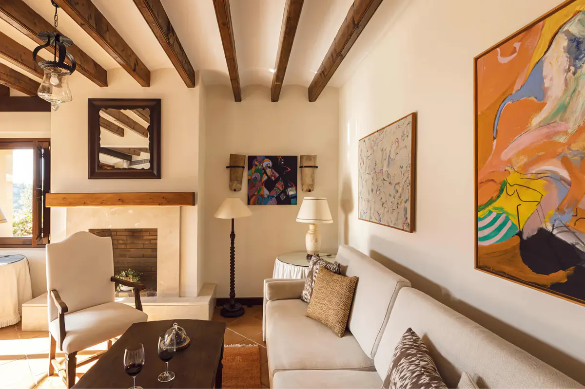 Living area with upholstered seating, framed artwork, exposed wooden beams, and stone fireplace