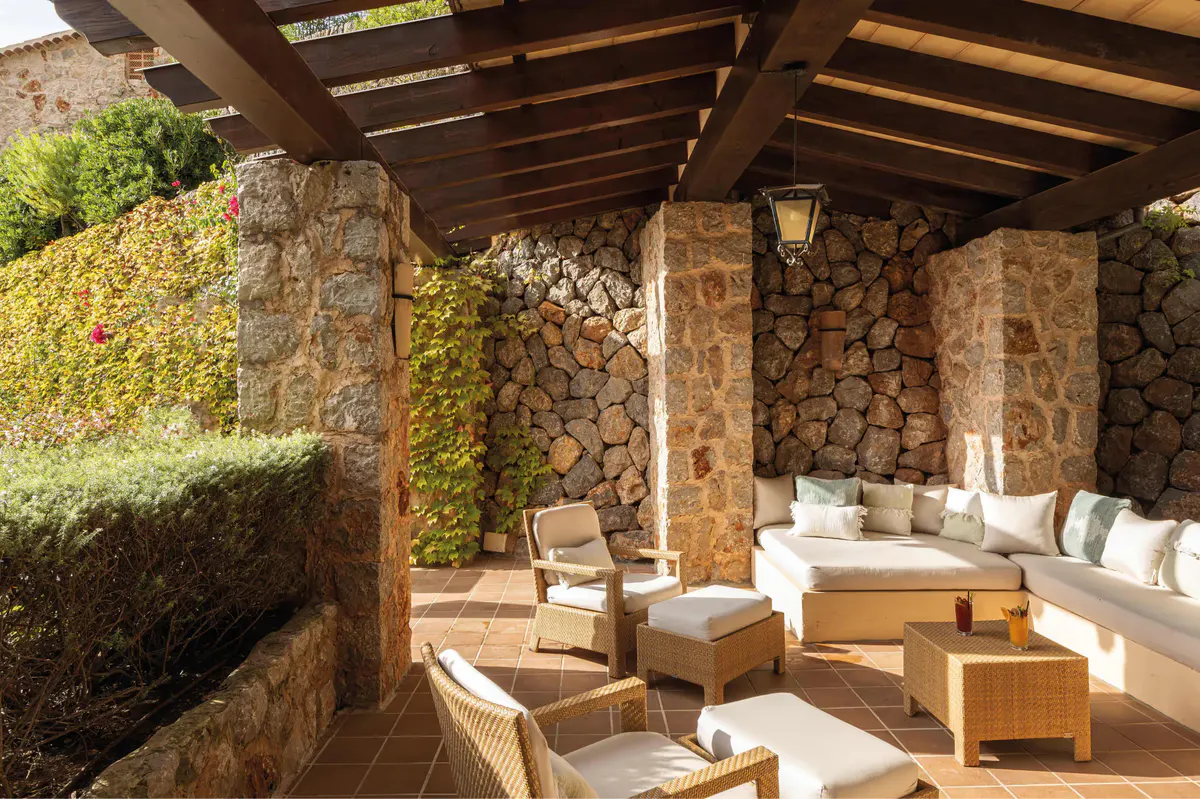 Covered patio with stone walls, wooden pergola, and cream-colored lounge seating
