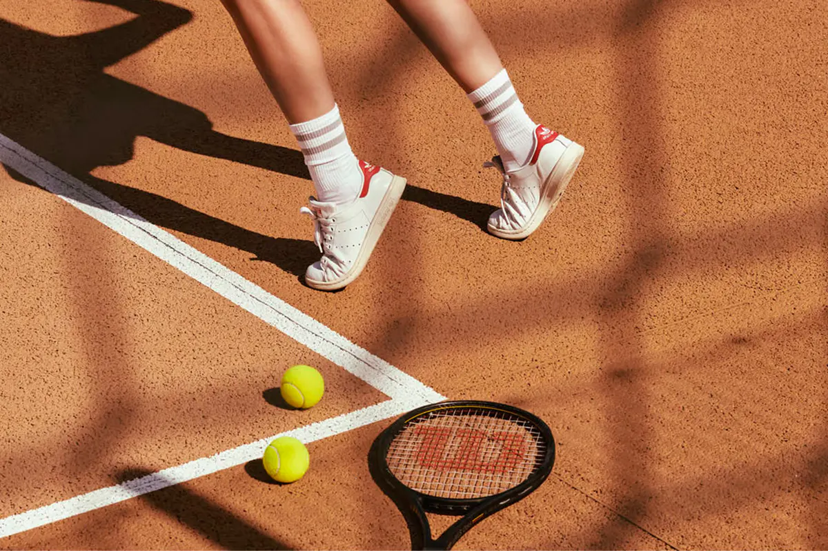 Tennis court with athletic shoes, racket, and bright yellow balls on rust-colored clay
