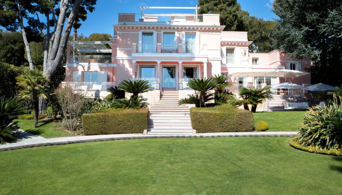 Pink and blue villa with manicured gardens and palm trees