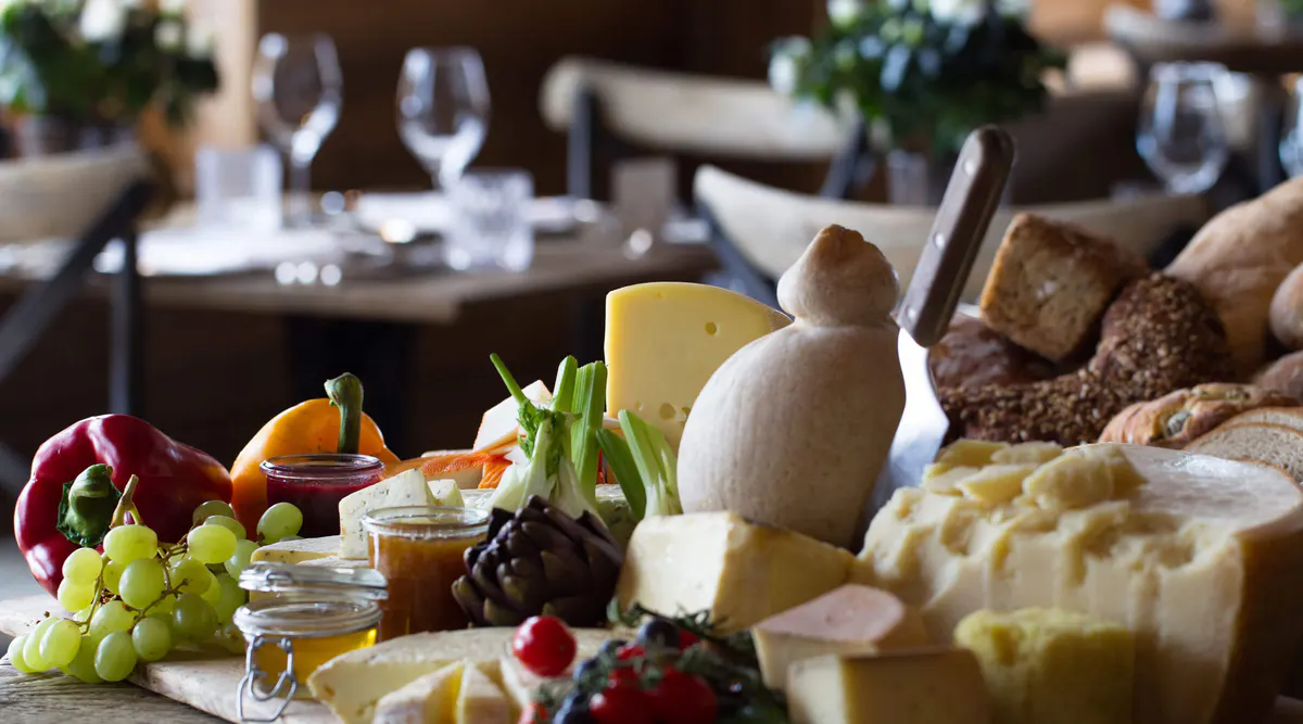 Plated cheese, fruit, and fresh produce with wine glasses in background