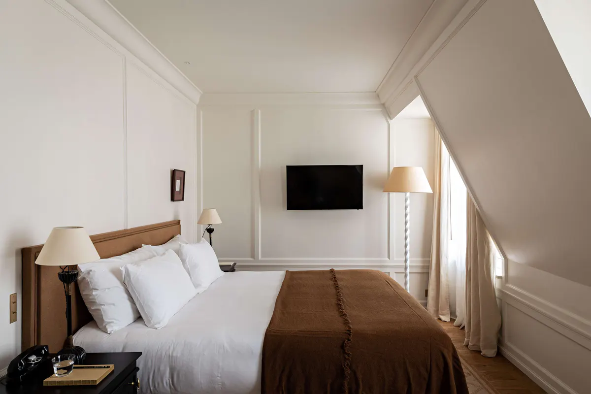 A bright bedroom with a wood platform bed, white pillows, and sloped ceiling