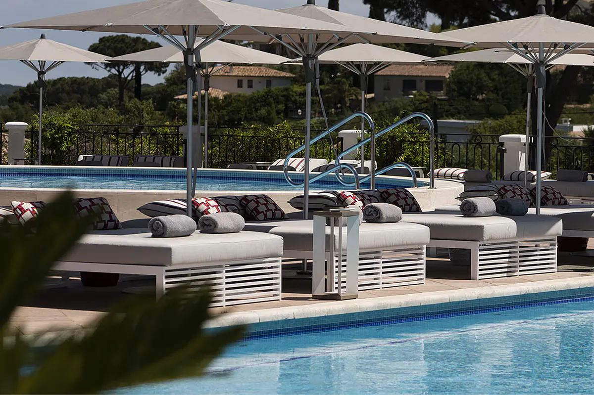 Shaded pool area with tan loungers and umbrellas on manicured grounds