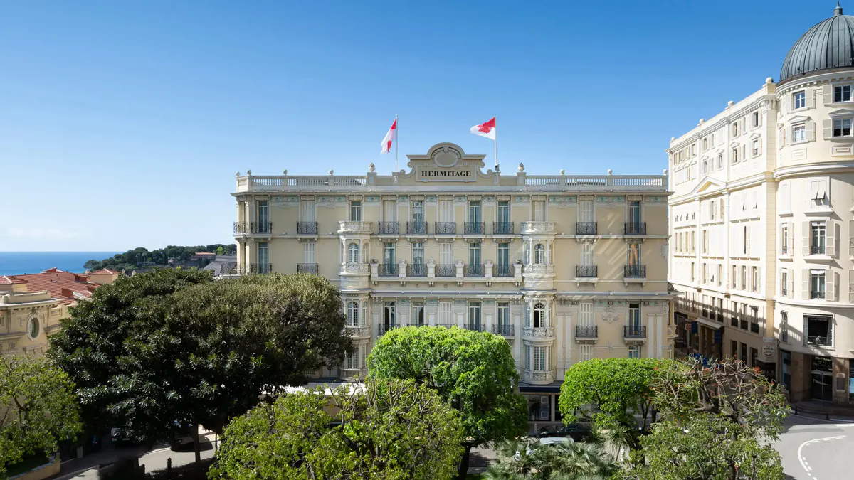 Pale stone palace building with French flags and formal public square below