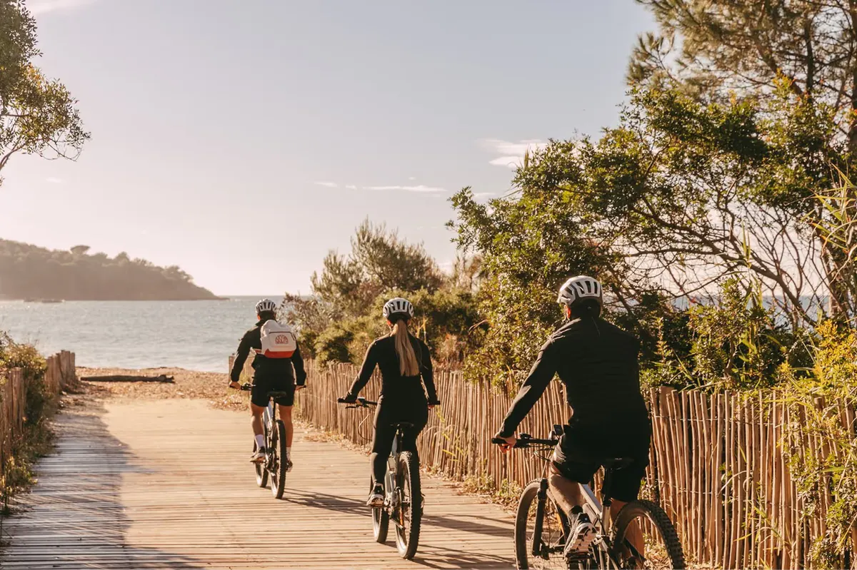 Cyclists on sandy beach path with sea and trees framing the route