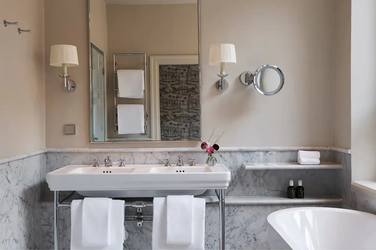 Bathroom with marble counter, dual sink, and circular mirror above vanity