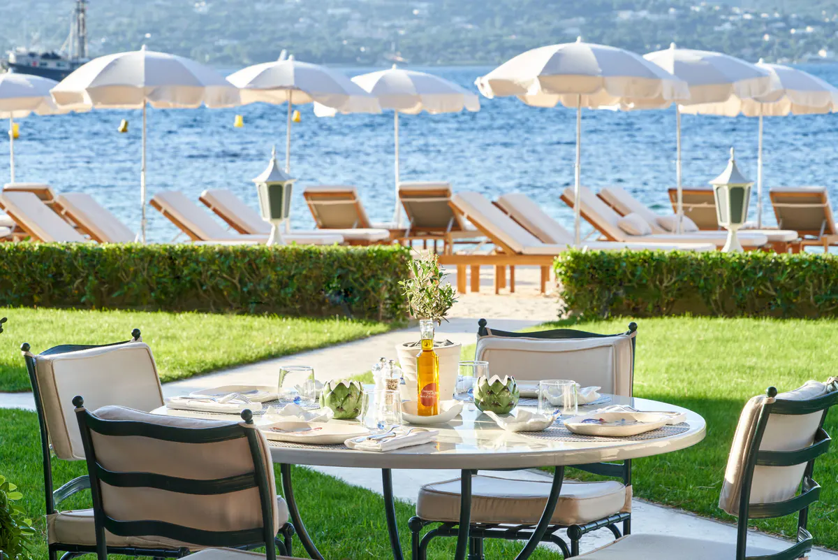 Grass terrace with round table and striped umbrellas overlooking bay