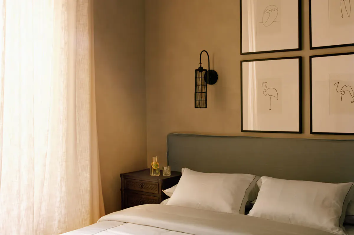 Bedroom with olive-green headboard, framed wall art, and warm incandescent lighting
