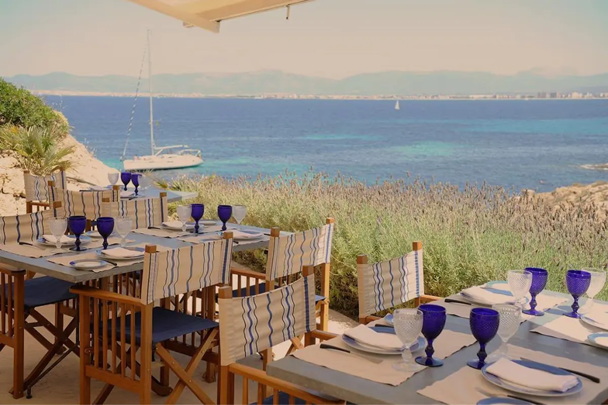 An intimate table for two on the beach at dusk, lit by brass lanterns and candlelight