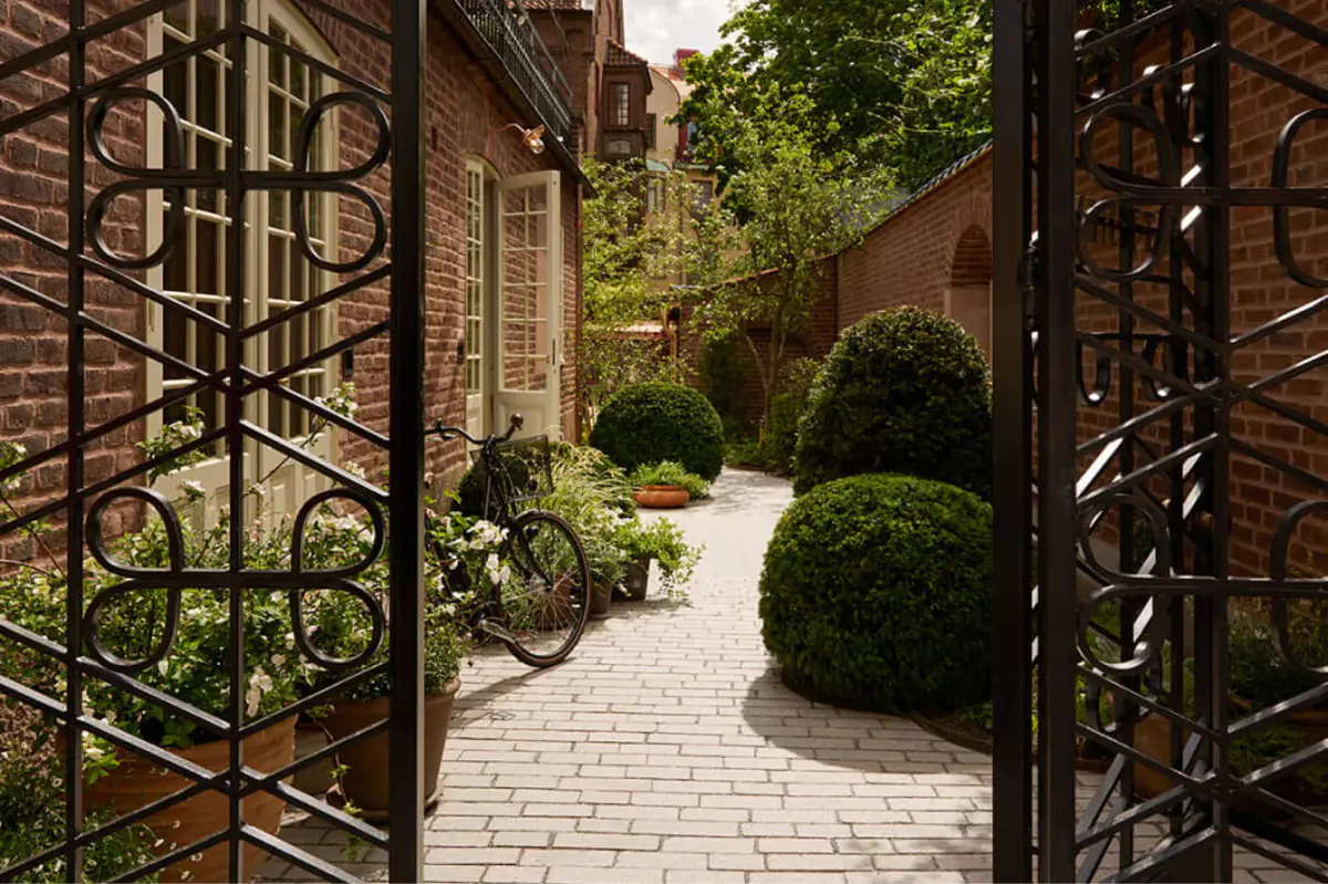 A garden pathway with ironwork gates, planted borders, and brick paving