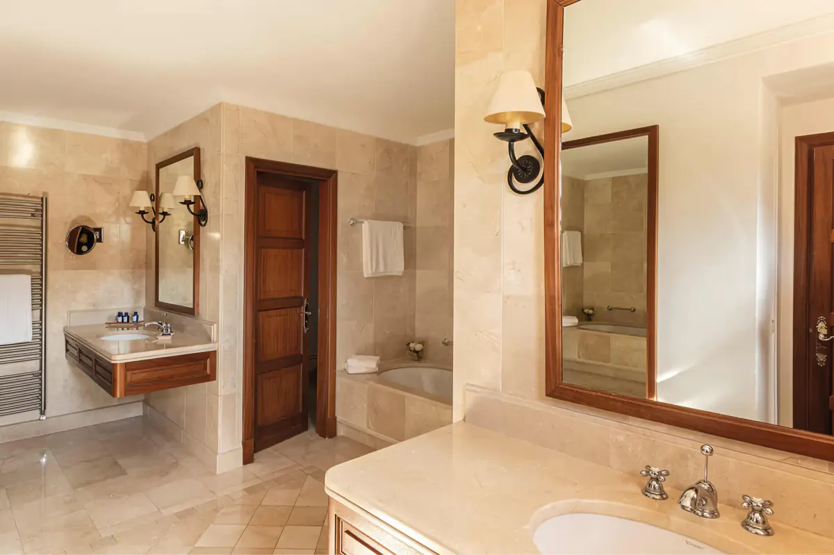 Spa-style bathroom with dual vanities, walk-in shower area, and warm natural stone finishes