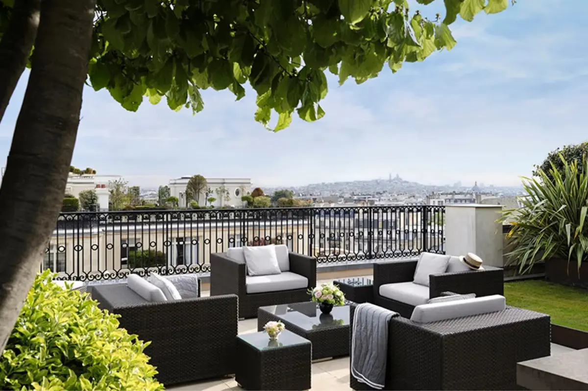 Rooftop terrace with shade trees, black lounge furniture, Paris cityscape, and overcast sky