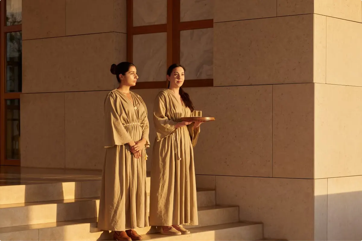 Spa therapists in neutral-toned robes in a sunlit corridor