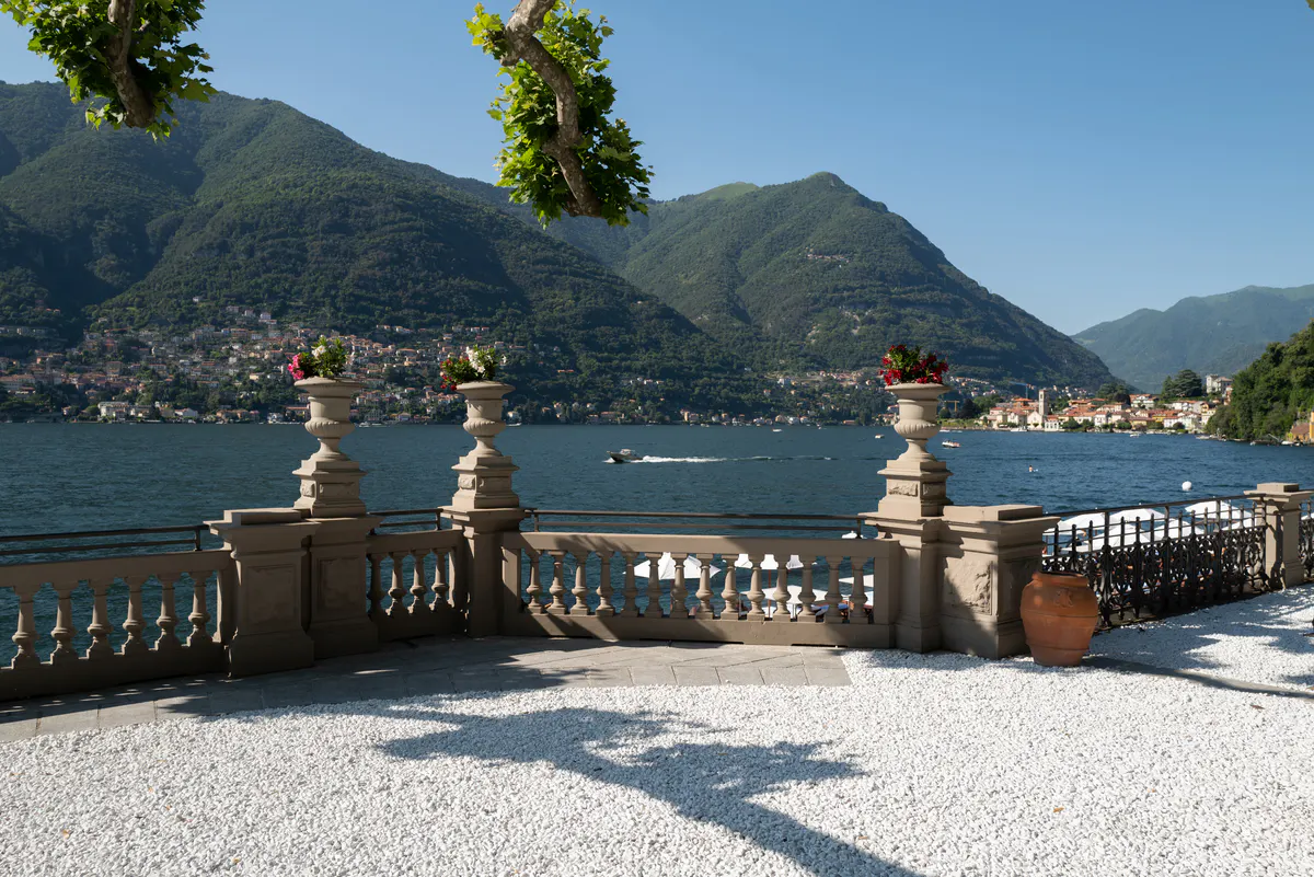 Terrace with three stone urns framing blue water, lakeside villages, and mountain vista