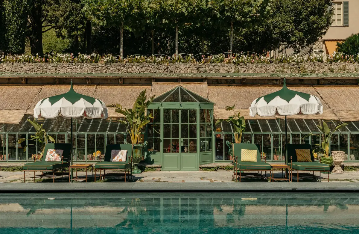 A stone terrace with loungers and white umbrellas beside a reflective pool
