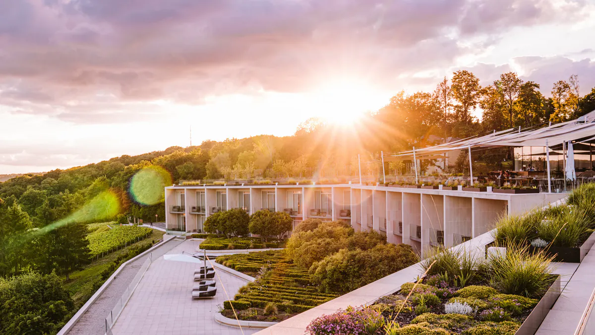 Modern hillside hotel with white facade and extensive glass windows overlooking vineyards at golden hour
