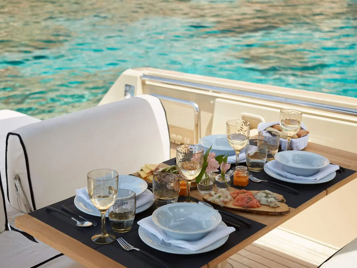A table setting on a boat overlooking turquoise waters, wine glasses, and blue dishware