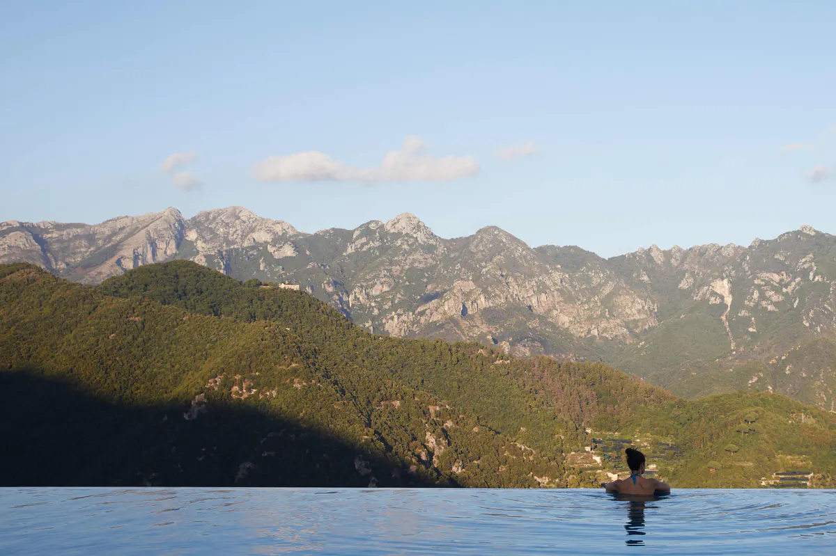 Swimmer in calm turquoise sea with forested mountains and distant coastline landscape