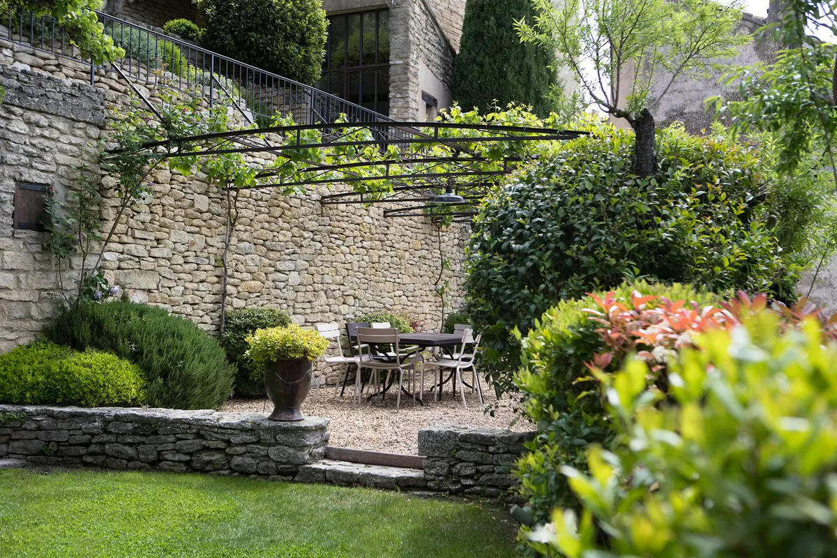 Garden terrace with stone walls, flowering plants, and metal furniture
