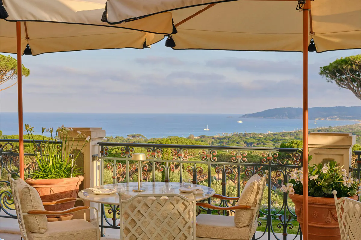 Outdoor dining table under cream canvas awning with rolled-up sides and distant sea horizon