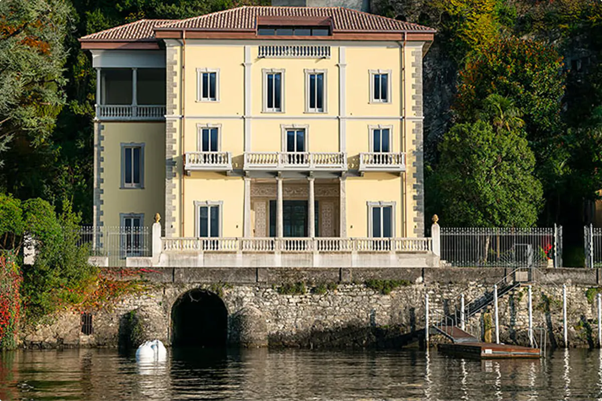 Pale yellow neoclassical villa with arched windows reflected in the lake