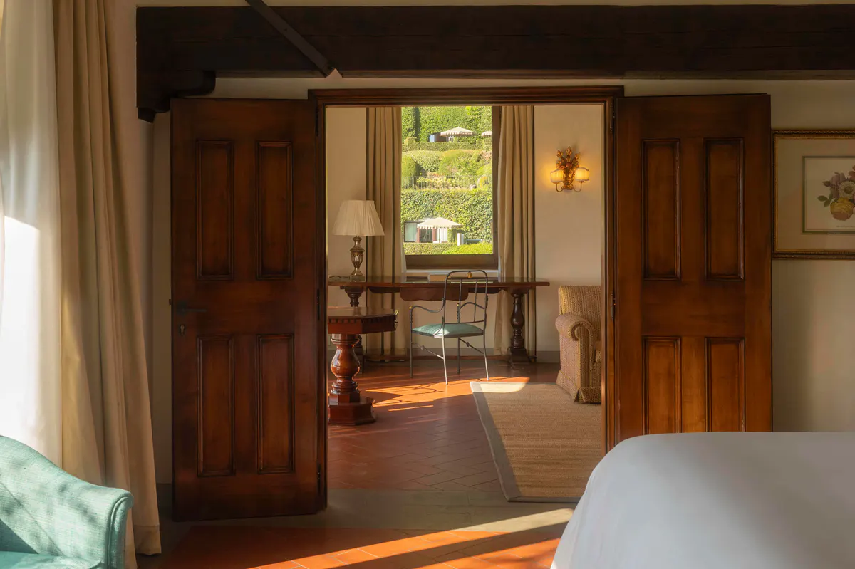 Dark wooden doors opening to a room with warm sunlight, beamed ceilings, and terracotta flooring