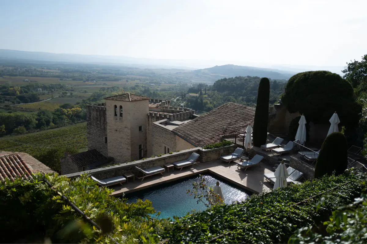 The hilltop village and stone buildings with a turquoise pool set below, overlooking sweeping countryside
