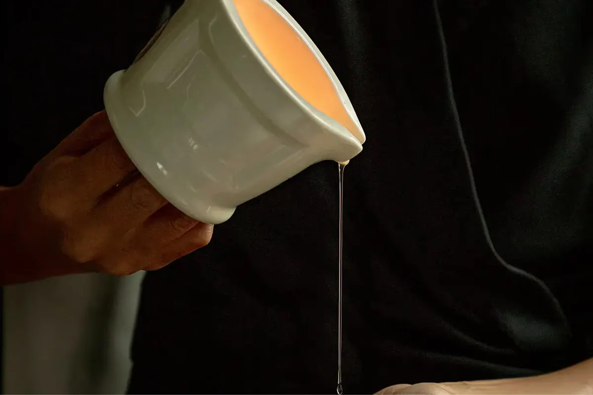 Hands pouring ritualistic hammam oil into ceramic bowl