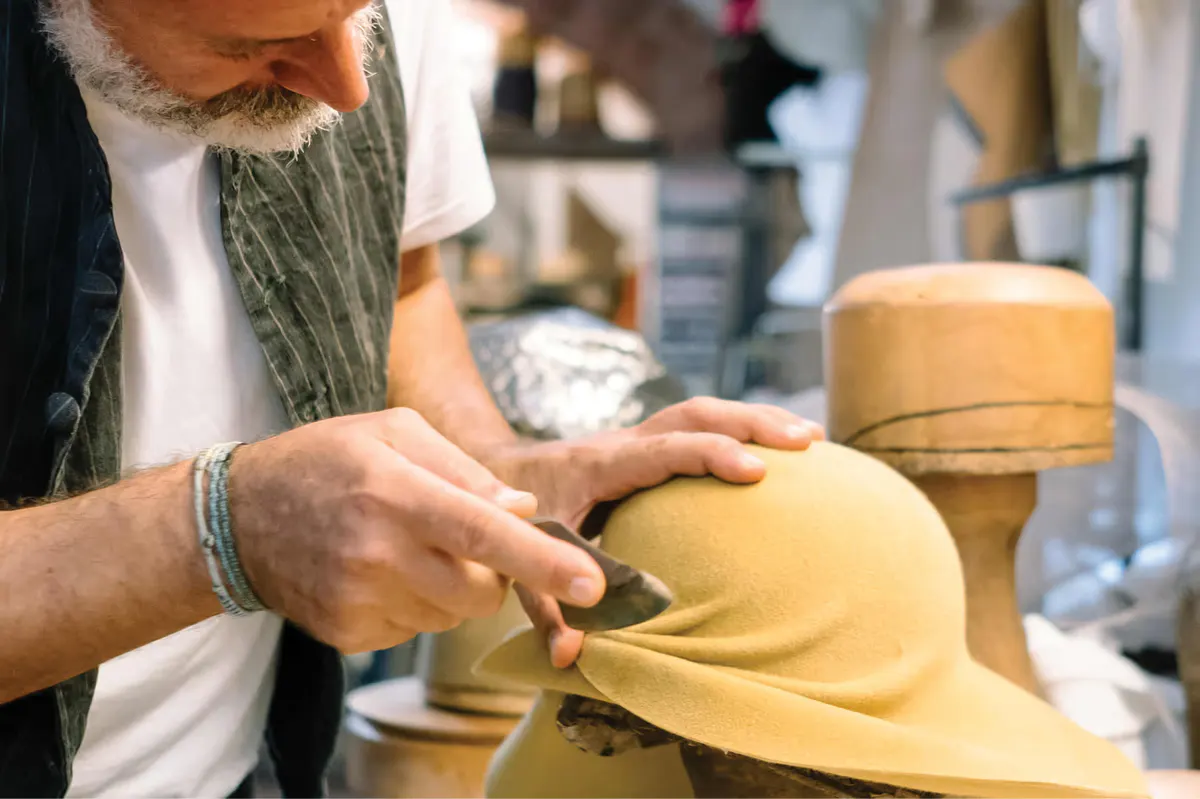 Hands shaping clay in a pottery workshop with craft materials on work surface