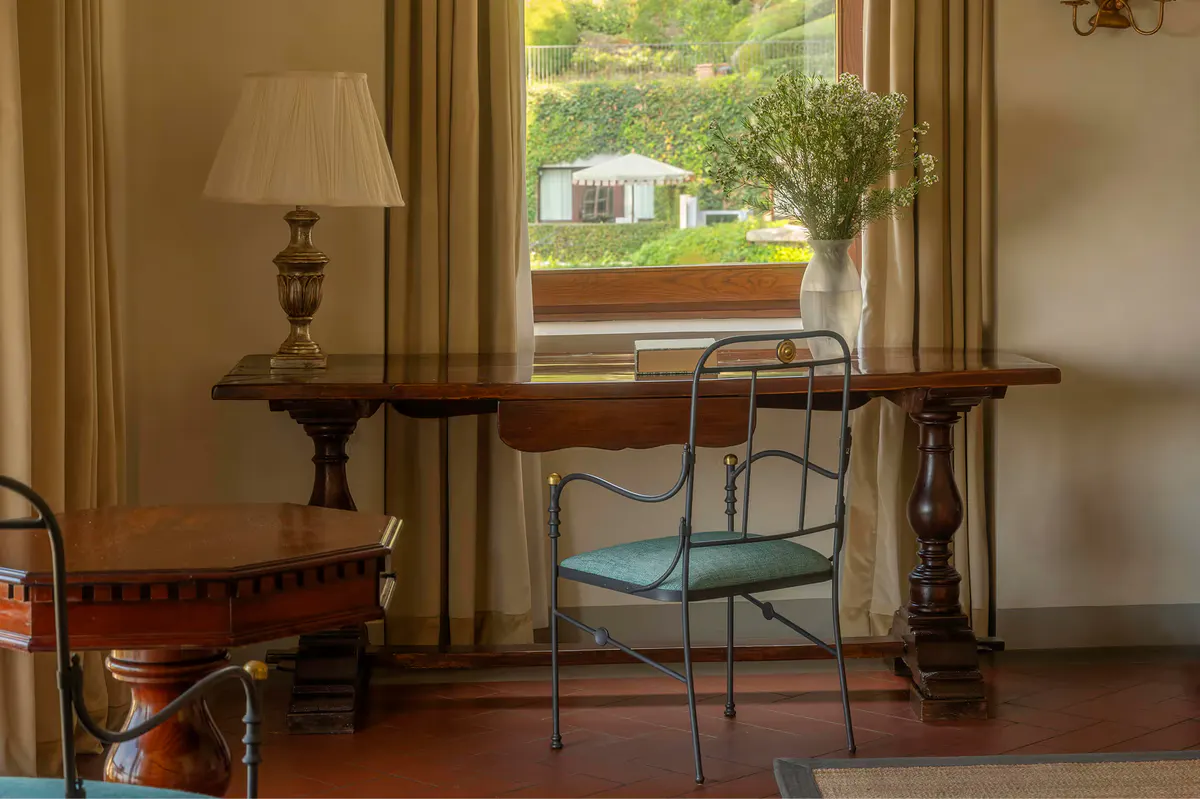 A study nook with wooden desk, green velvet chair, and view to gardens and grounds