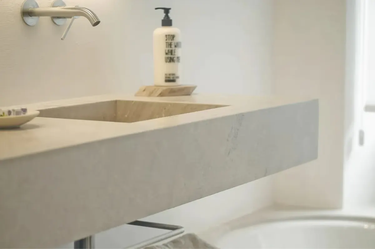 Minimalist concrete vanity with integrated sink, brass fixtures, and natural side lighting