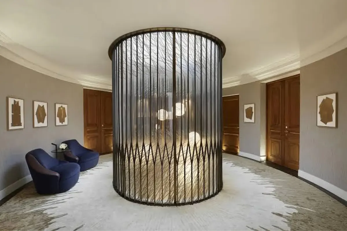 A curved cylindrical black metal sculpture in a foyer with blue armchair and cream walls
