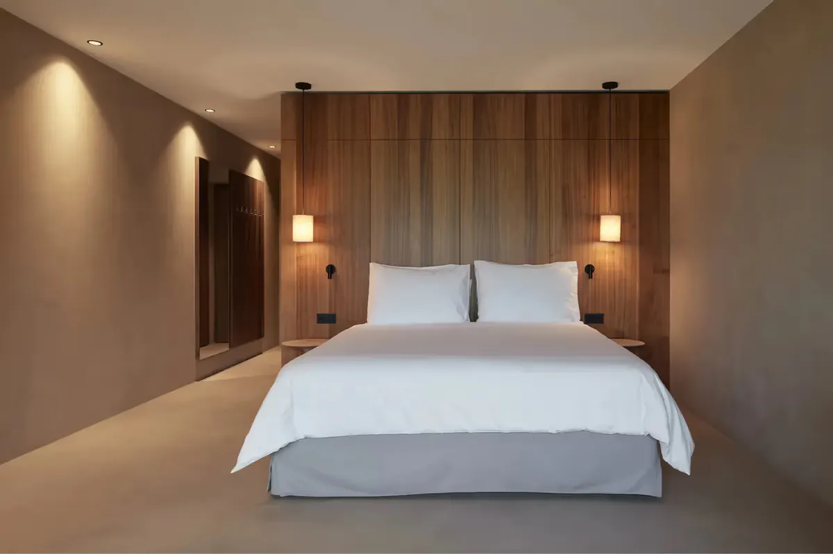 Modern bedroom with white bed and warm wood headboard wall under soft recessed lighting
