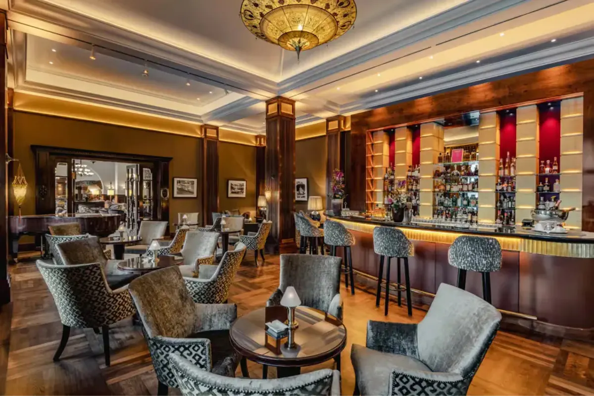 A bar lounge with coffered ceiling, upholstered seating, and shelves of spirits and wines