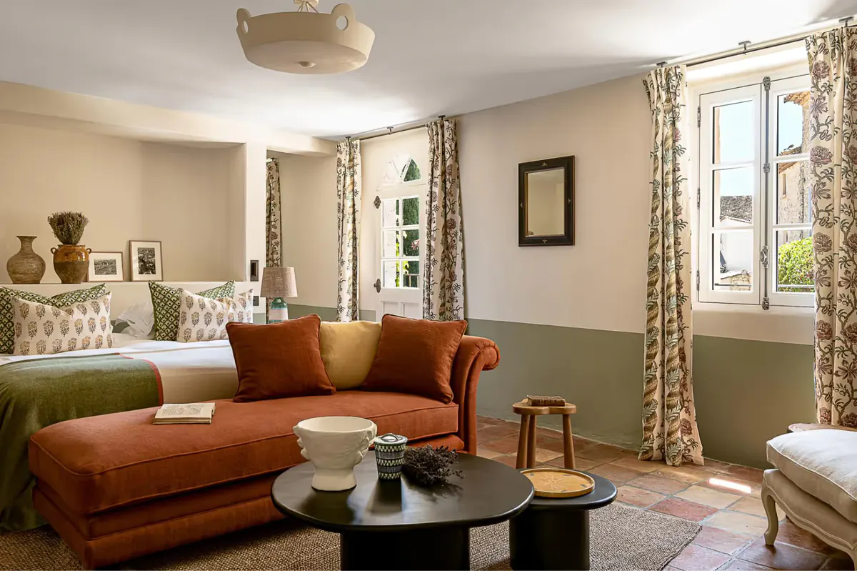 A sitting room with a rust-colored velvet sofa, mustard pillows, and green wall sections opposite a bed