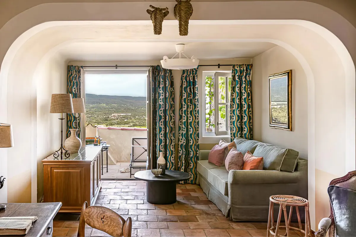 A room with an arched alcove bathing area, green patterned curtains, and countryside views through arched windows