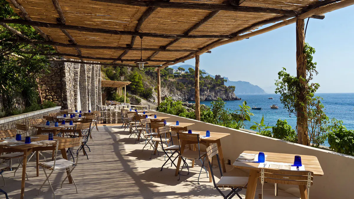 Casual beachside trattoria with wooden tables and coastal mountain views