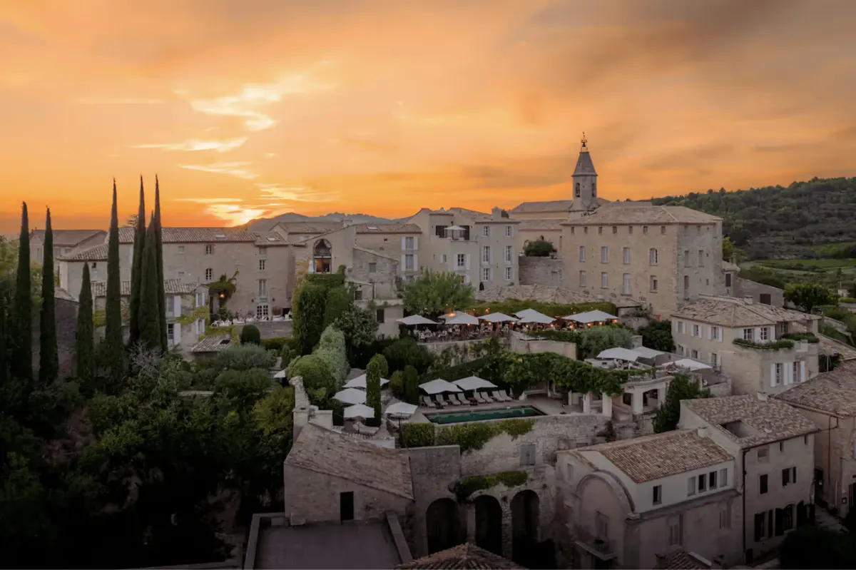 The hilltop village at sunset with golden light, stone architecture, and cypress trees against the landscape