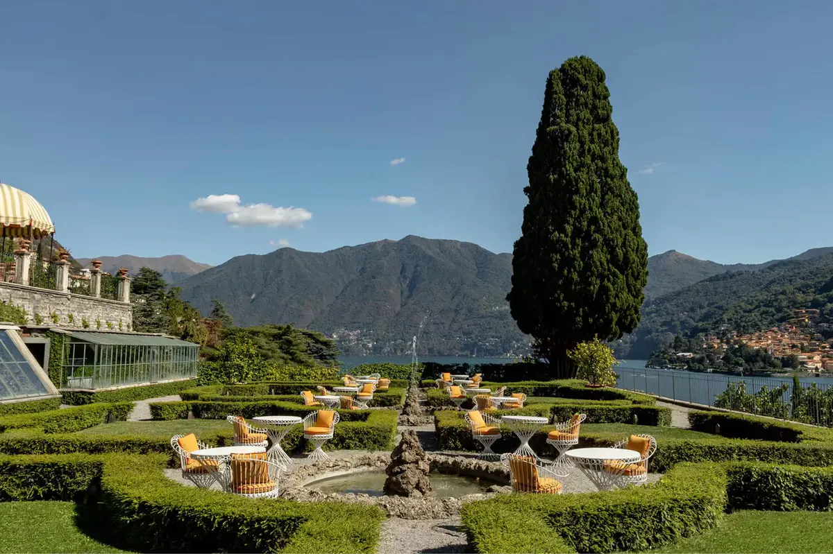 Manicured grounds with tall cypress, scattered seating, and lake views beyond hedges
