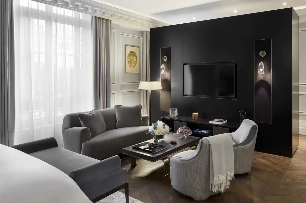 A living room with black accent wall, television, dark furniture, and light drapes framing tall windows