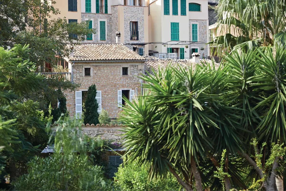 Stone buildings with green shutters set among palm and cypress trees in village setting