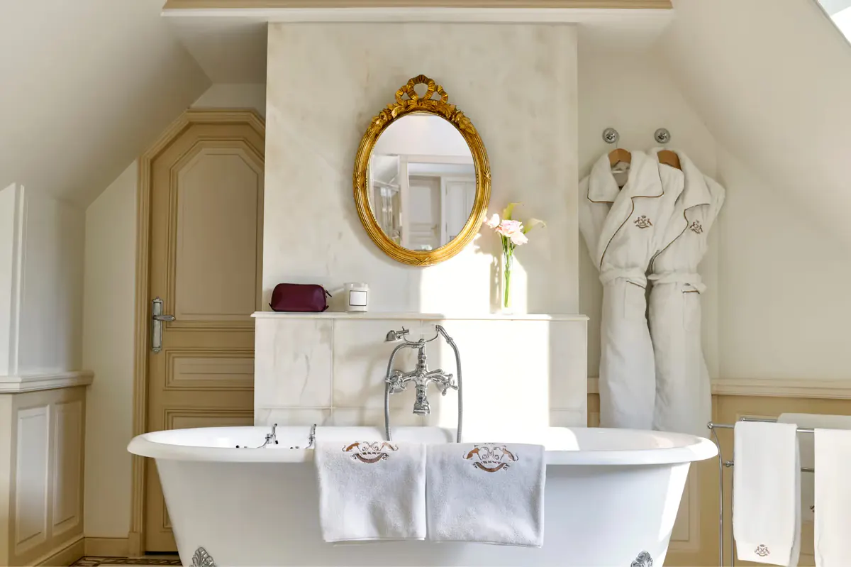 A bathroom with freestanding white marble tub and gilt-framed mirror and classical details