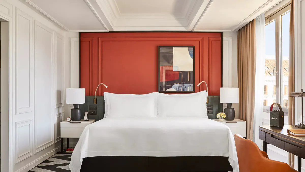 A bedroom with a red upholstered headboard, white bedding, and mirrored walls