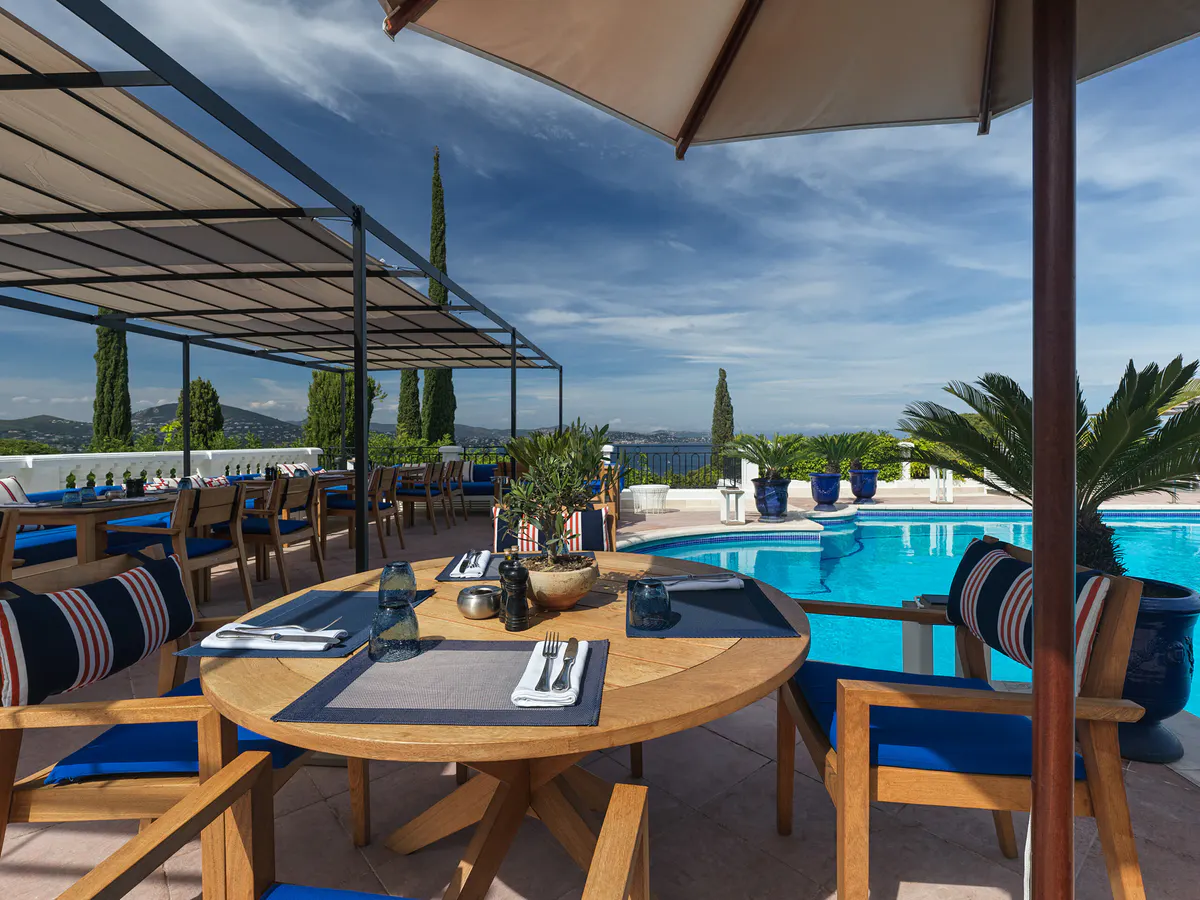 Waterside terrace dining area with striped cushions overlooking the pools
