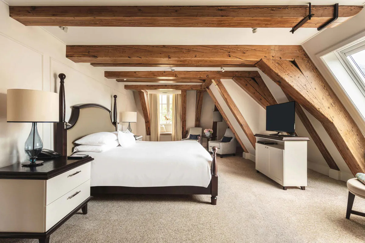 An attic bedroom with exposed timber beams, sloped ceilings, a black platform bed, and soft natural light