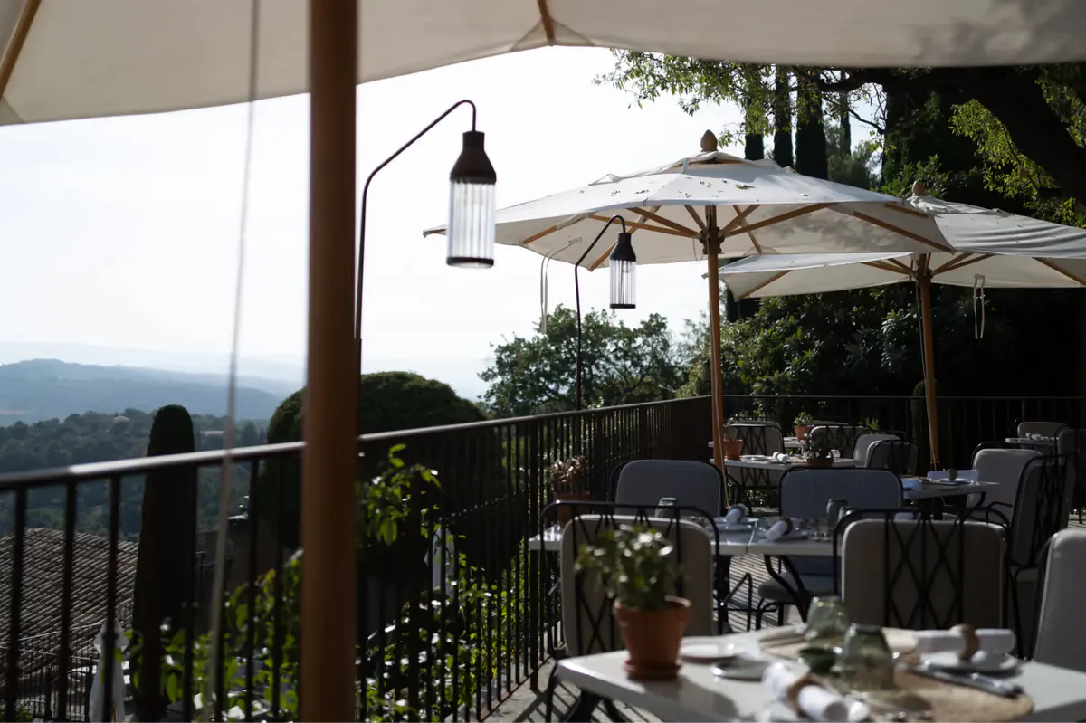 An outdoor terrace with table service, white umbrellas, and distant mountain views at a restaurant
