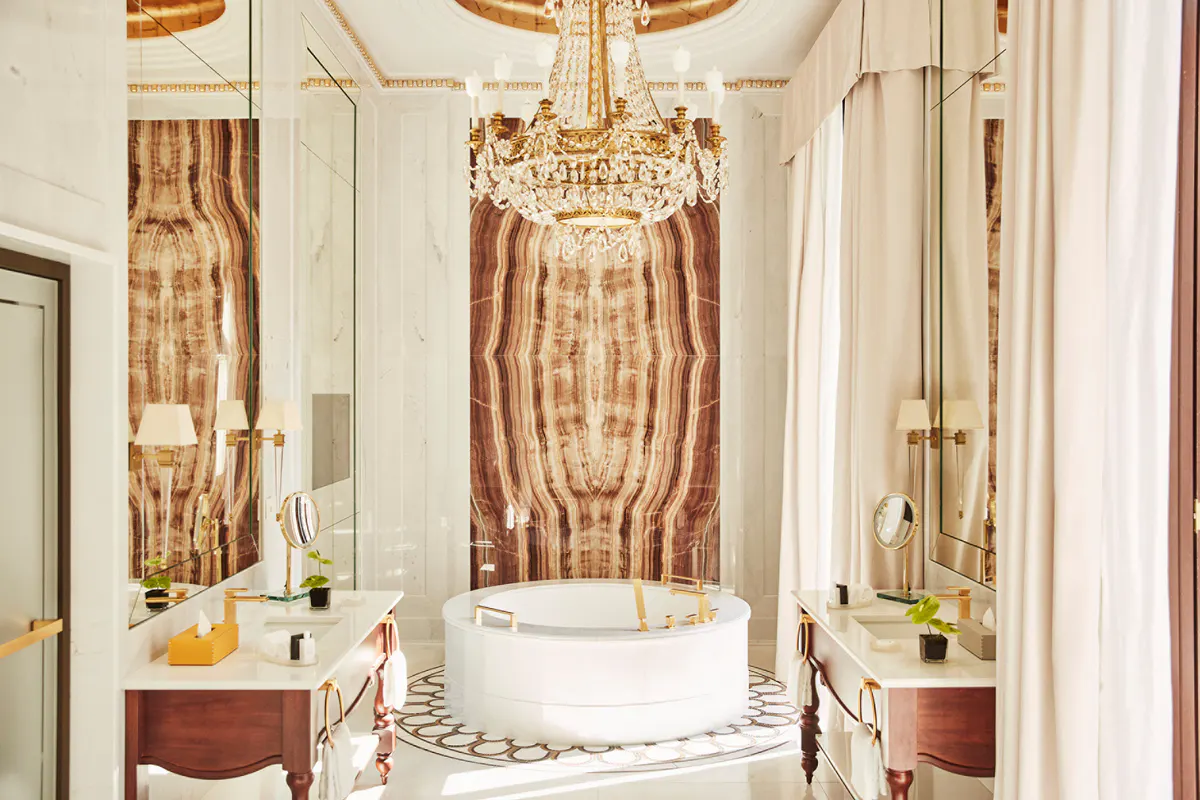 Spa bathroom with crystal chandelier, marble tub surround, brass fixtures, and ornate gold accents