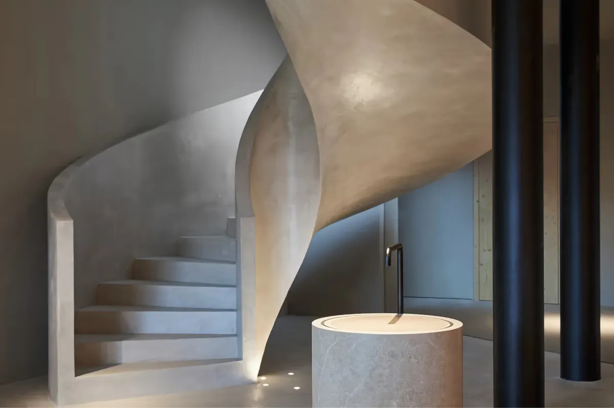 A sculptural spiral staircase in light concrete with natural wood framing and black metal railings