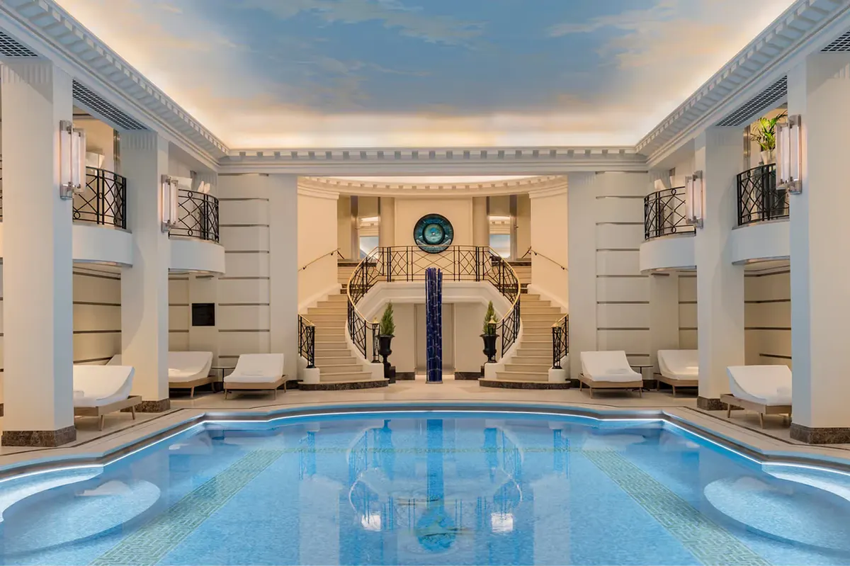 The indoor swimming pool with pale stone walls, arched alcoves, and recessed lighting