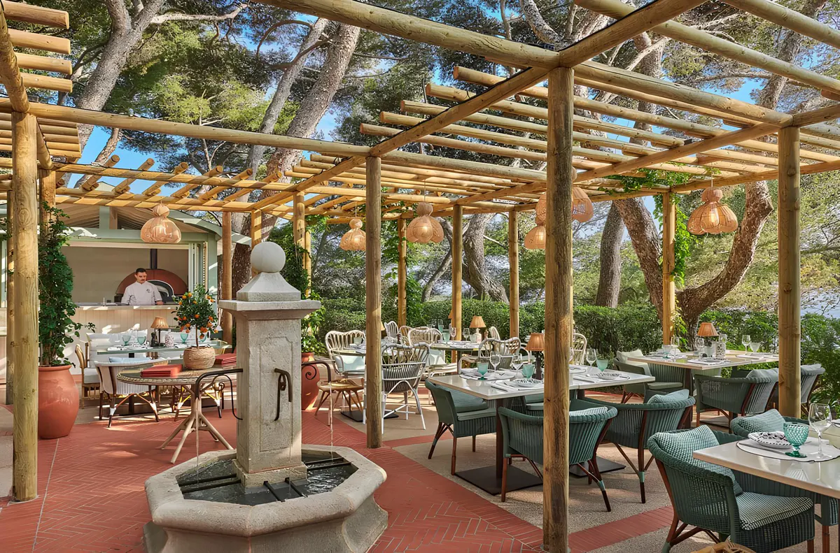 A covered outdoor restaurant with pergola structure, woven furnishings, and Mediterranean setting
